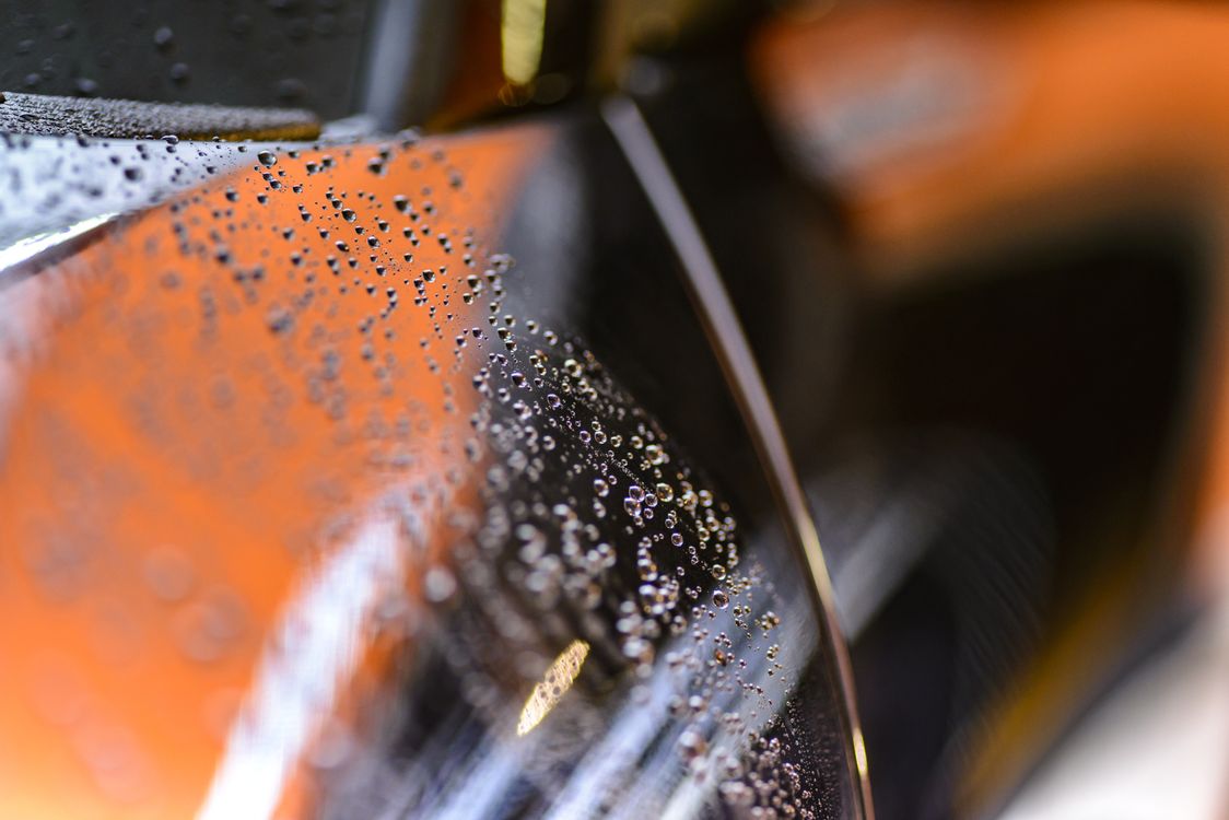 Water beading tightly on a freshly coated dark car panel.