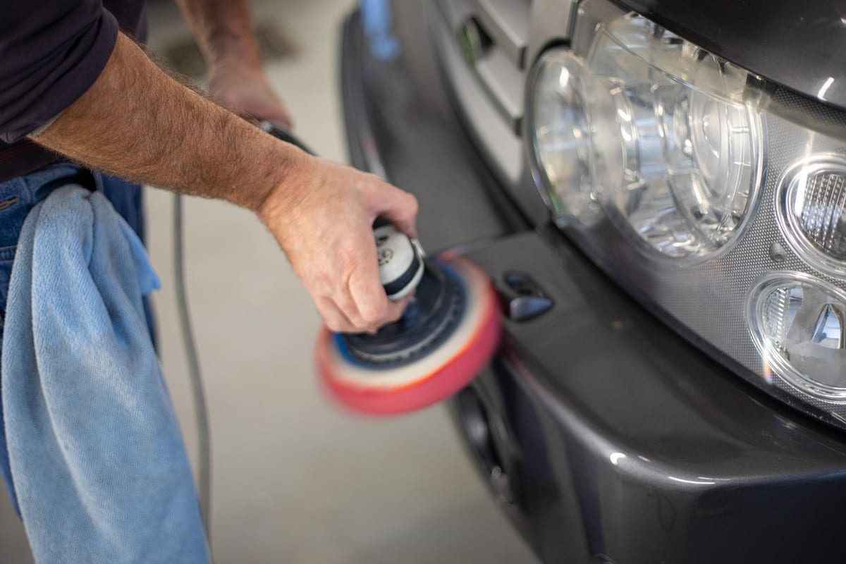Gloved hands running a dual-action polisher with a red pad across a car's panel.
