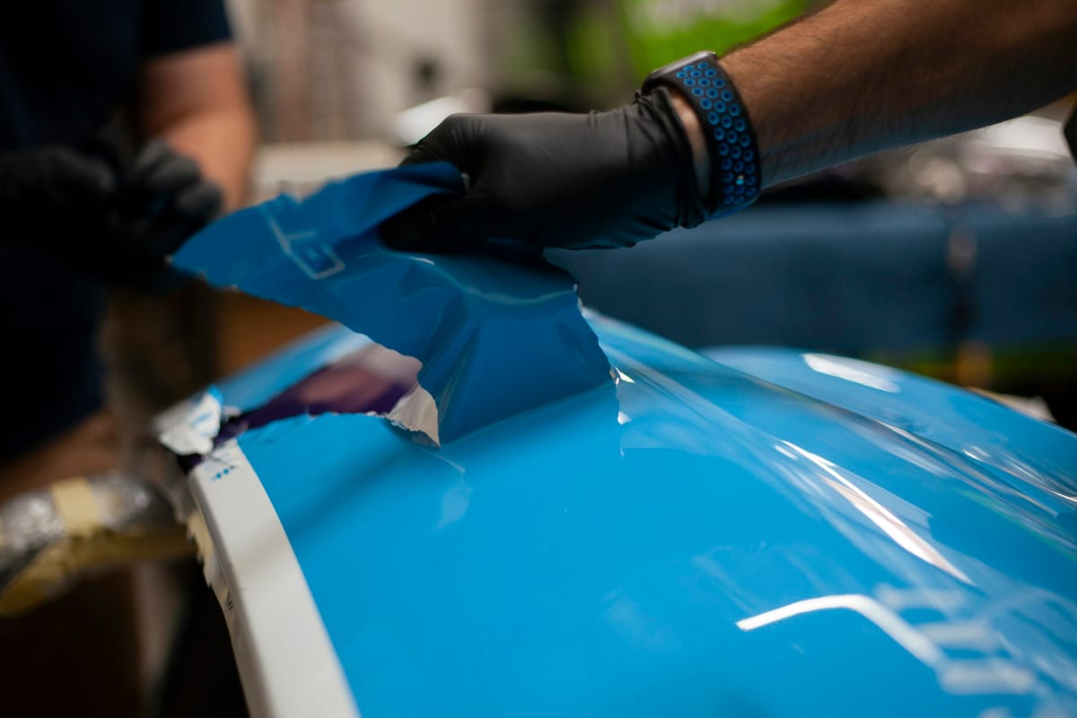 A technician laying protective film onto a blue-panelled car body.