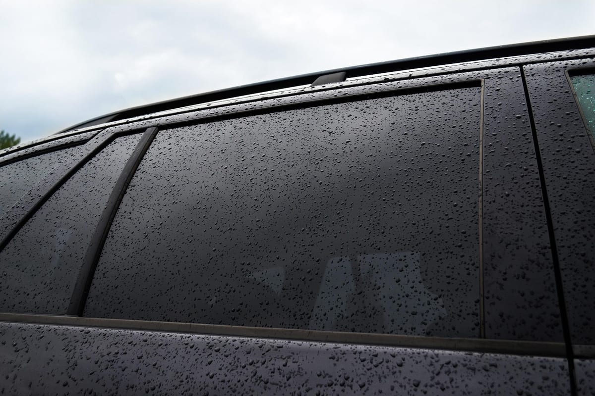 Close-up of rain-speckled dark tinted rear side windows on a car, showing the uniformly dark glass a mid-to-premium film tier produces.