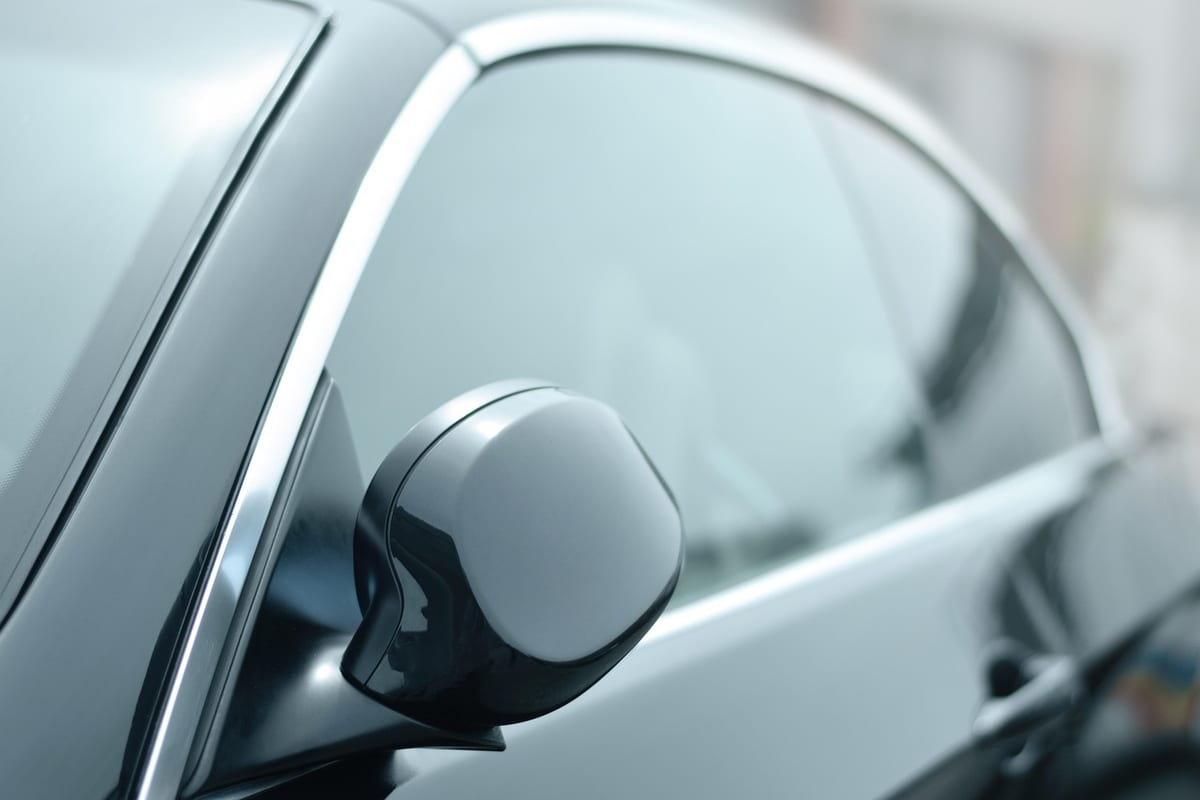 Close-up of a light-tinted car side window and black side mirror, showing the mild factory-level tint most cars start with before an aftermarket film goes on.